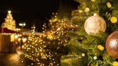 European Christmas city with festive fair or market in the evening. Christmas tree with beautiful balls on foreground. Holiday background.
