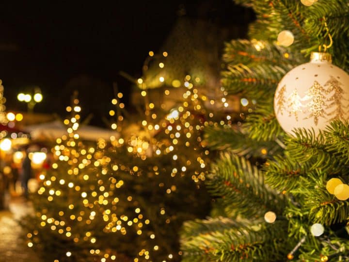 European Christmas city with festive fair or market in the evening. Christmas tree with beautiful balls on foreground. Holiday background.